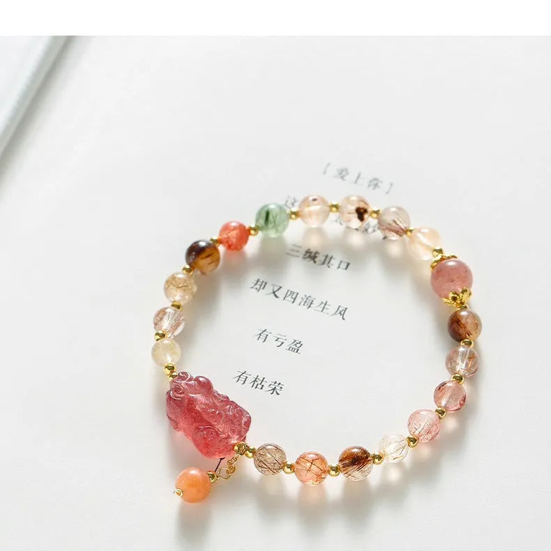 Copper women's bracelet with a pink Strawberry Quartz crystal and a gold-toned Pixiu charm, alongside smaller crystal beads.