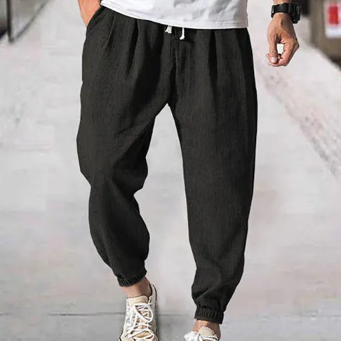 Man wearing loose light-coloured cotton trousers with elasticated ankle cuffs, showing front and side views.