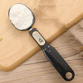 White digital kitchen scale with LCD display and spoon-shaped weighing surface for precise ingredient measurements