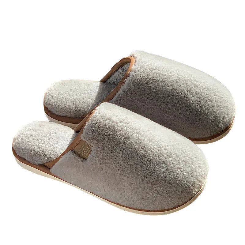 A pair of solid colour winter plush slippers with a PVC sole on a wooden floor.