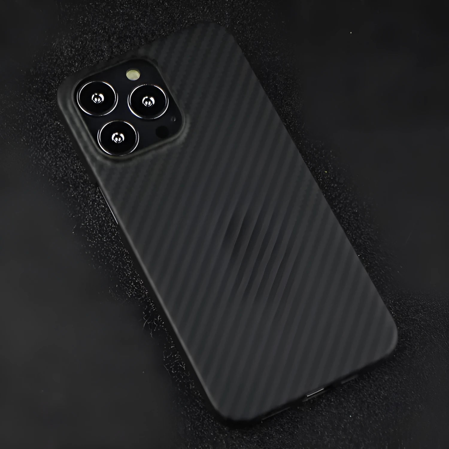 Dull black Kevlar iPhone case with volcanic crater texture next to a MagSafe charger.