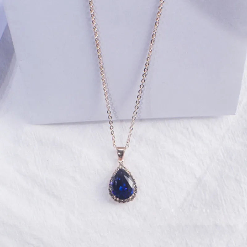 Close-up of a women's rose gold tone drop pendant necklace with pink rhinestone inlay on a model.