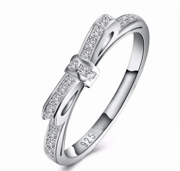 Silver bow-shaped ring with sparkling rhinestones and zircon crystals on a finger.