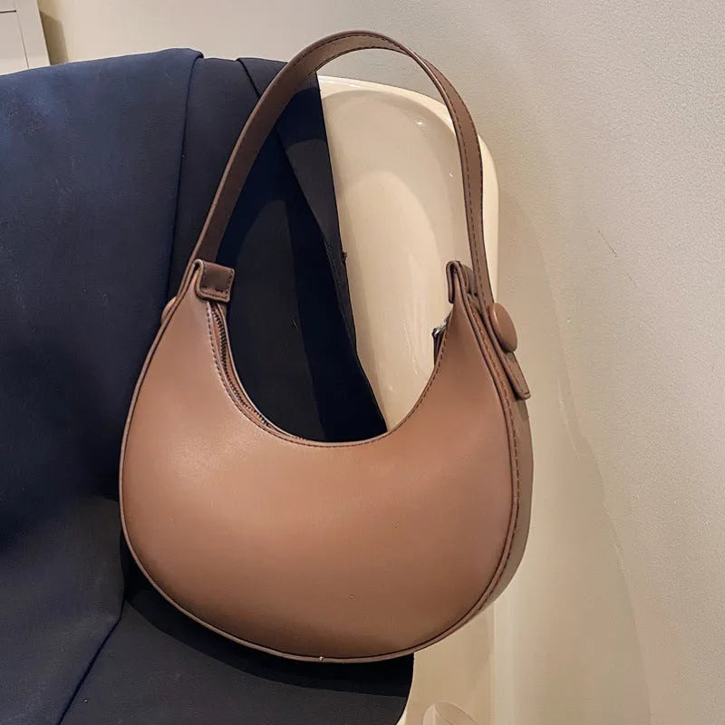 Women's retro-style PU dumpling shoulder bag in black, showing front zipper compartment.