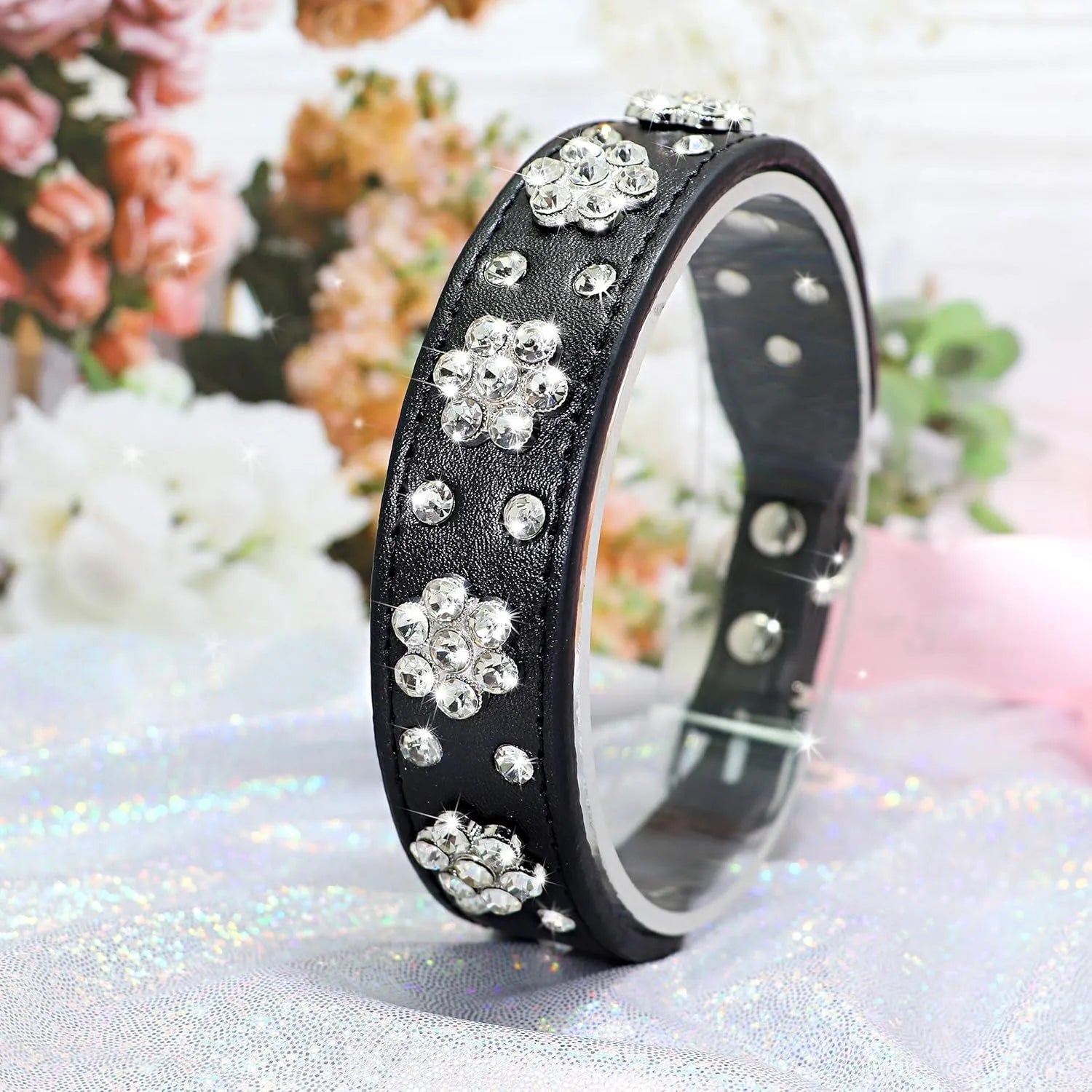 Close-up of a black PU leather dog collar with sparkling rhinestone flower studs and a metal D-ring