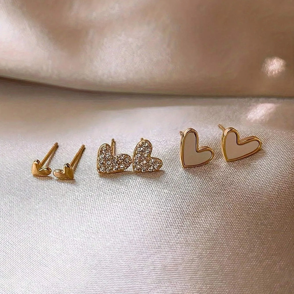 Three pairs of women's heart-shaped earrings in gold, black, black and white, and pink colours