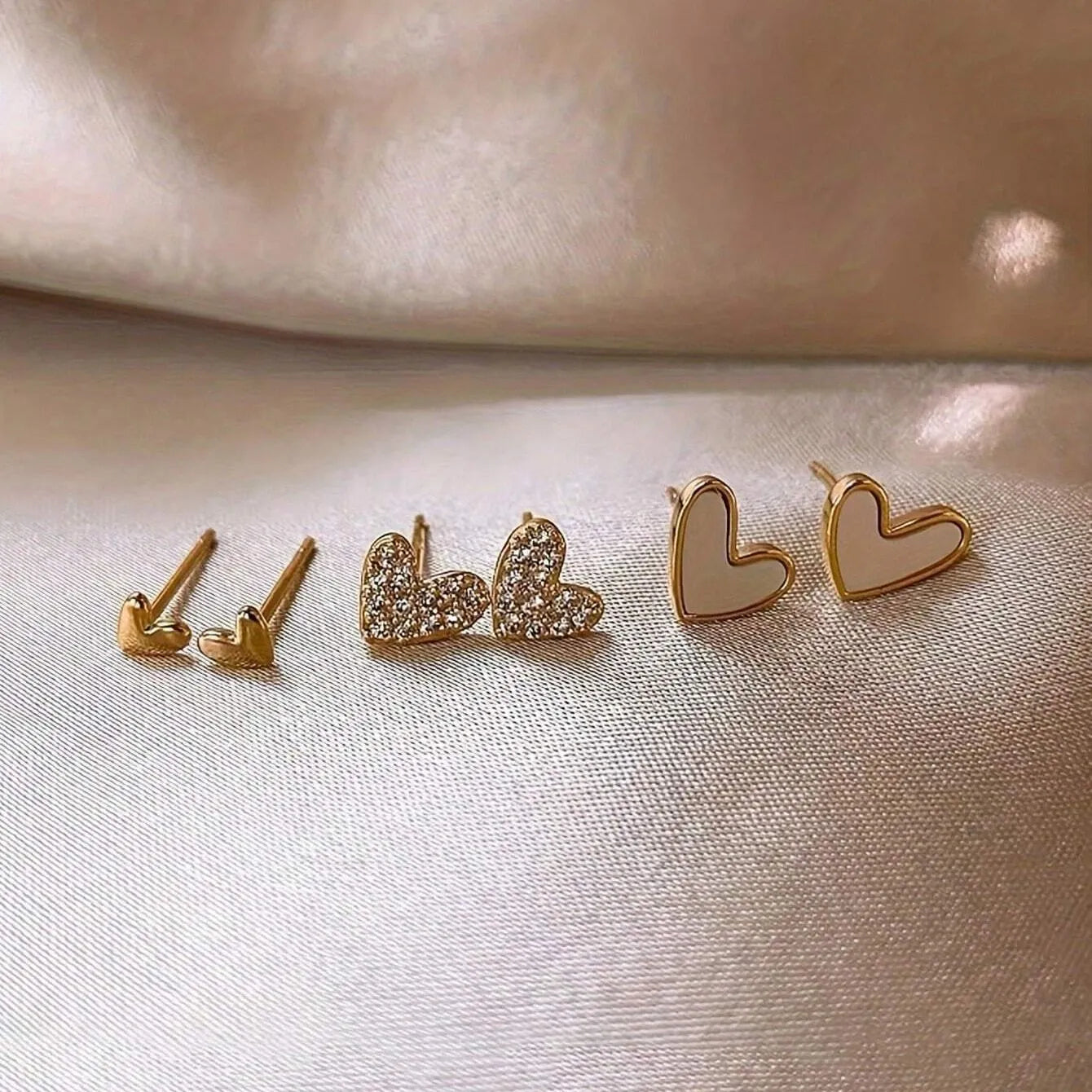 Three pairs of women's heart-shaped earrings in gold, black, black and white, and pink colours