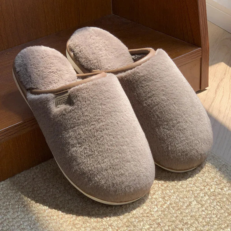A pair of solid colour winter plush slippers with a PVC sole on a wooden floor.