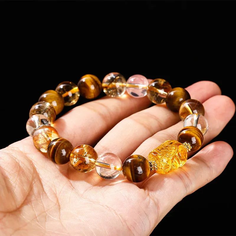 Close-up of a yellow tiger's eye and citrine bead bracelet with a geometric pi xiu charm on a wrist.