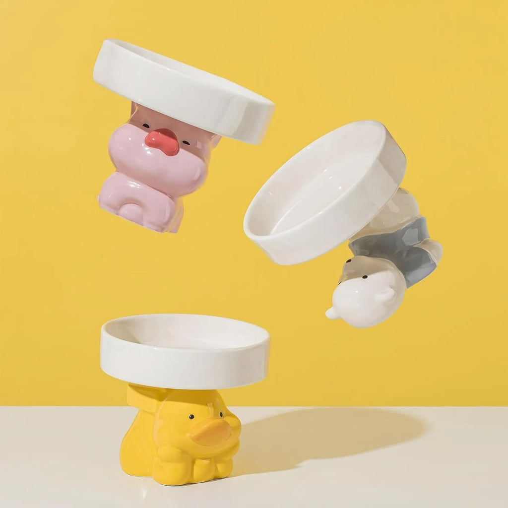 White ceramic raised cat bowl with a bear design, showing its elevated stand and wide feeding dish.
