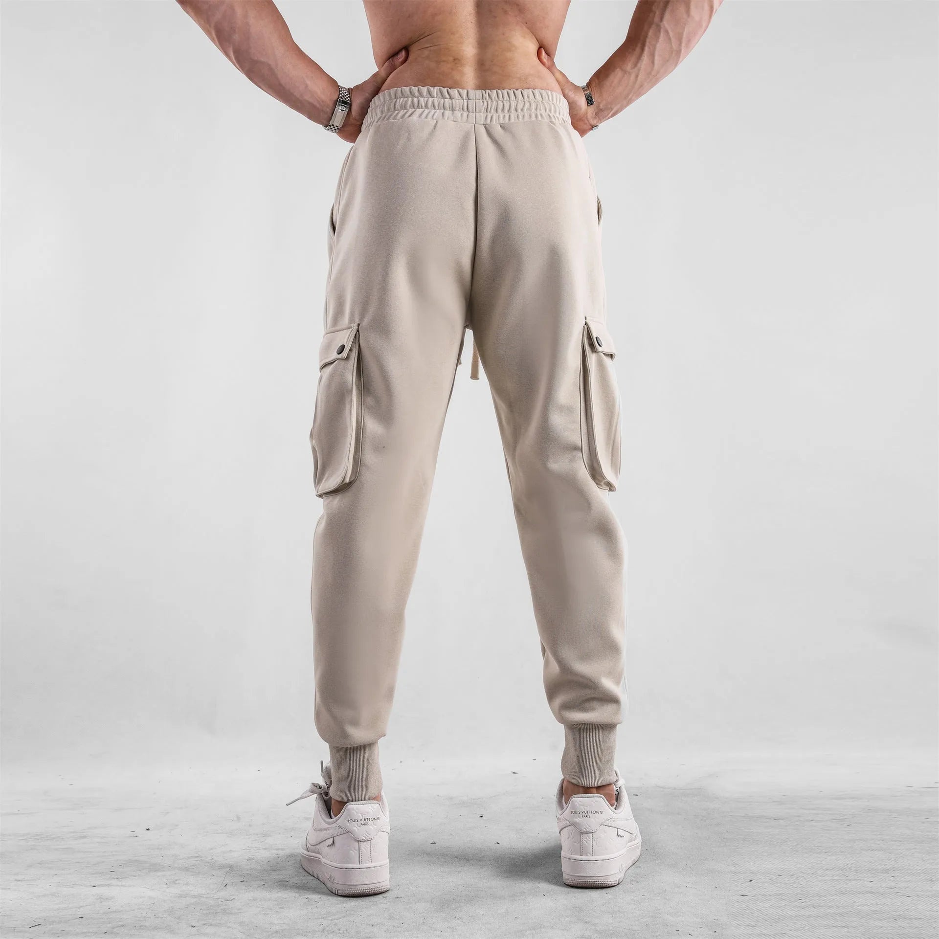 Men's loose-fit beige cotton sports trousers with ankle ties and side pockets laid flat.