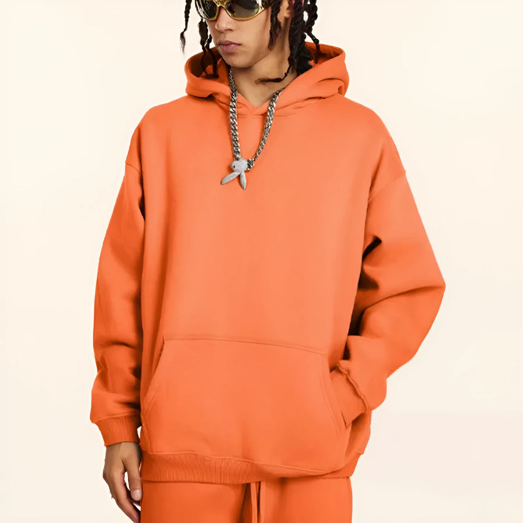A man wearing a loose grey hooded cotton terry sweater with drop-shoulder sleeves.