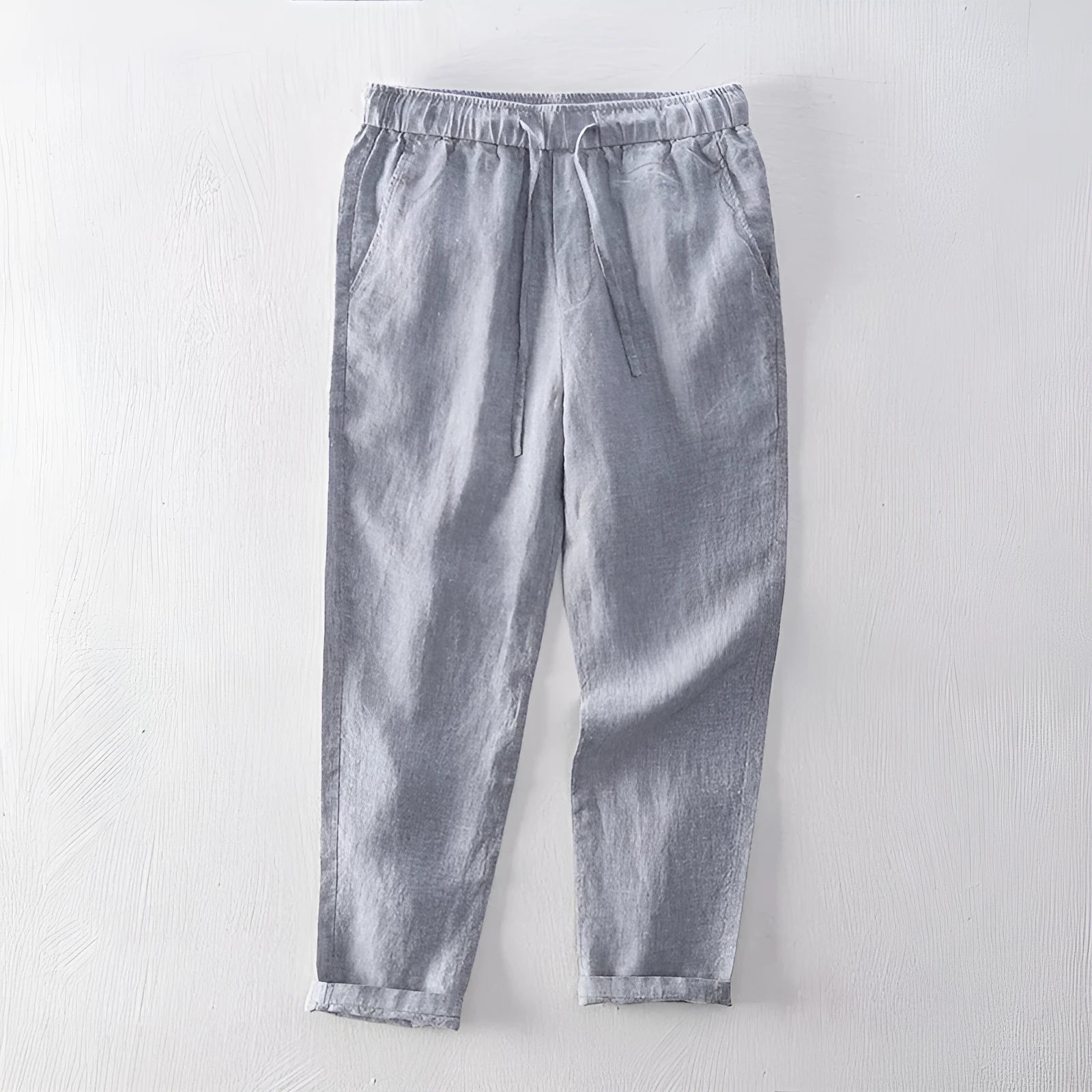 Men's straight-leg linen trousers in light grey, laid flat to show the mid-waist and tailored cut.