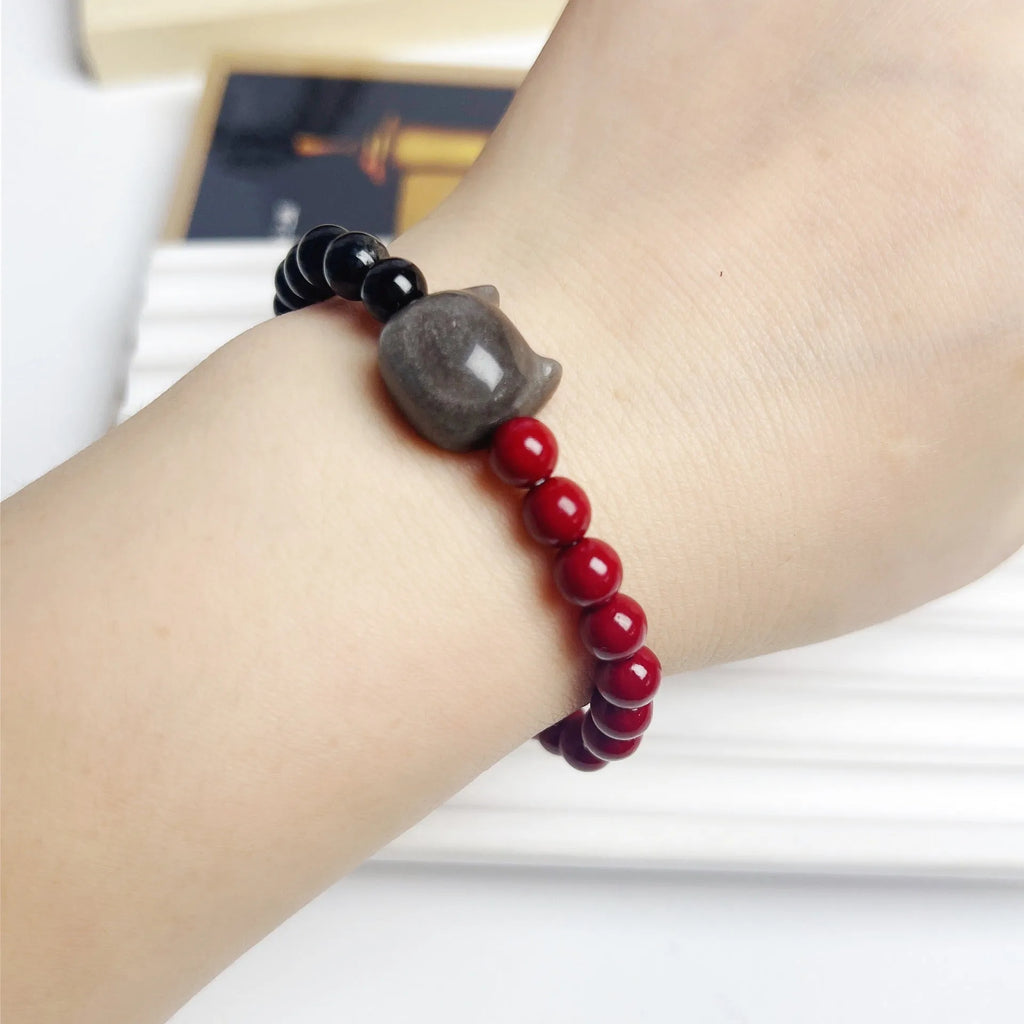 Close-up of handmade obsidian-colour bead bracelet with metal cat charm on adjustable red string.