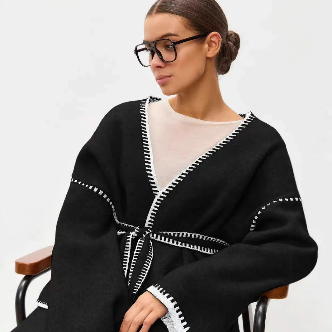 A white lace-up knitted cardigan with long sleeves on a hanger, showing the front tie detail.
