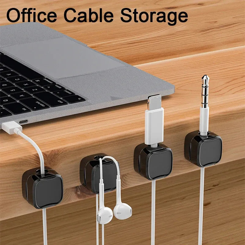 White and black magnetic cable clips with adhesive backing holding a USB cable against a wooden desk edge.