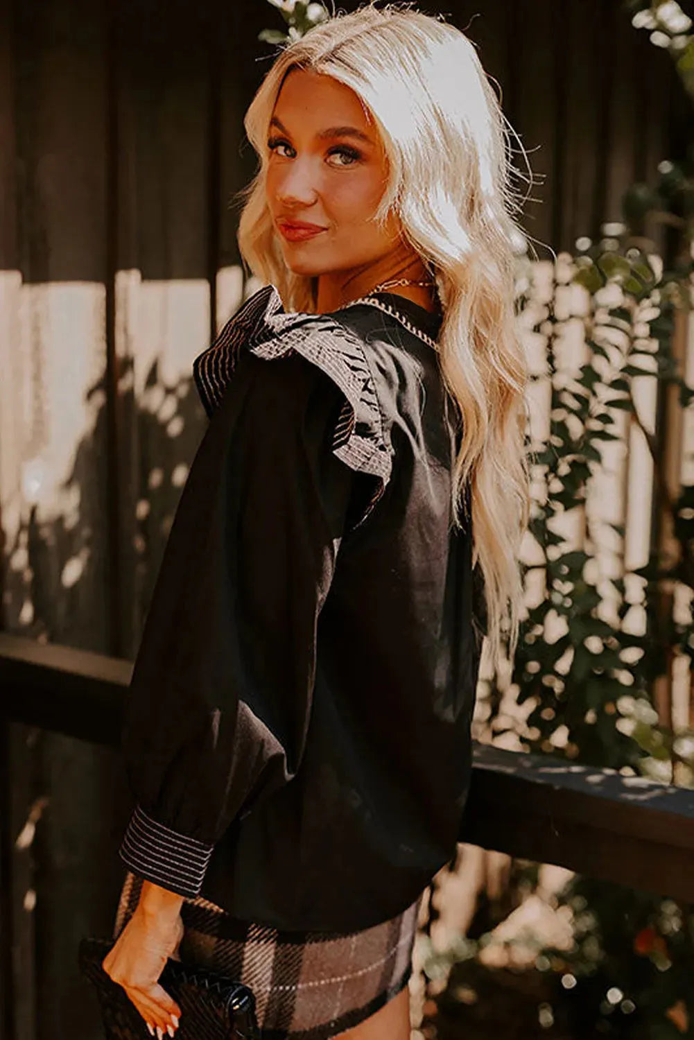 Black V-neck long sleeve blouse with a decorative ruffle and contrast stitching.