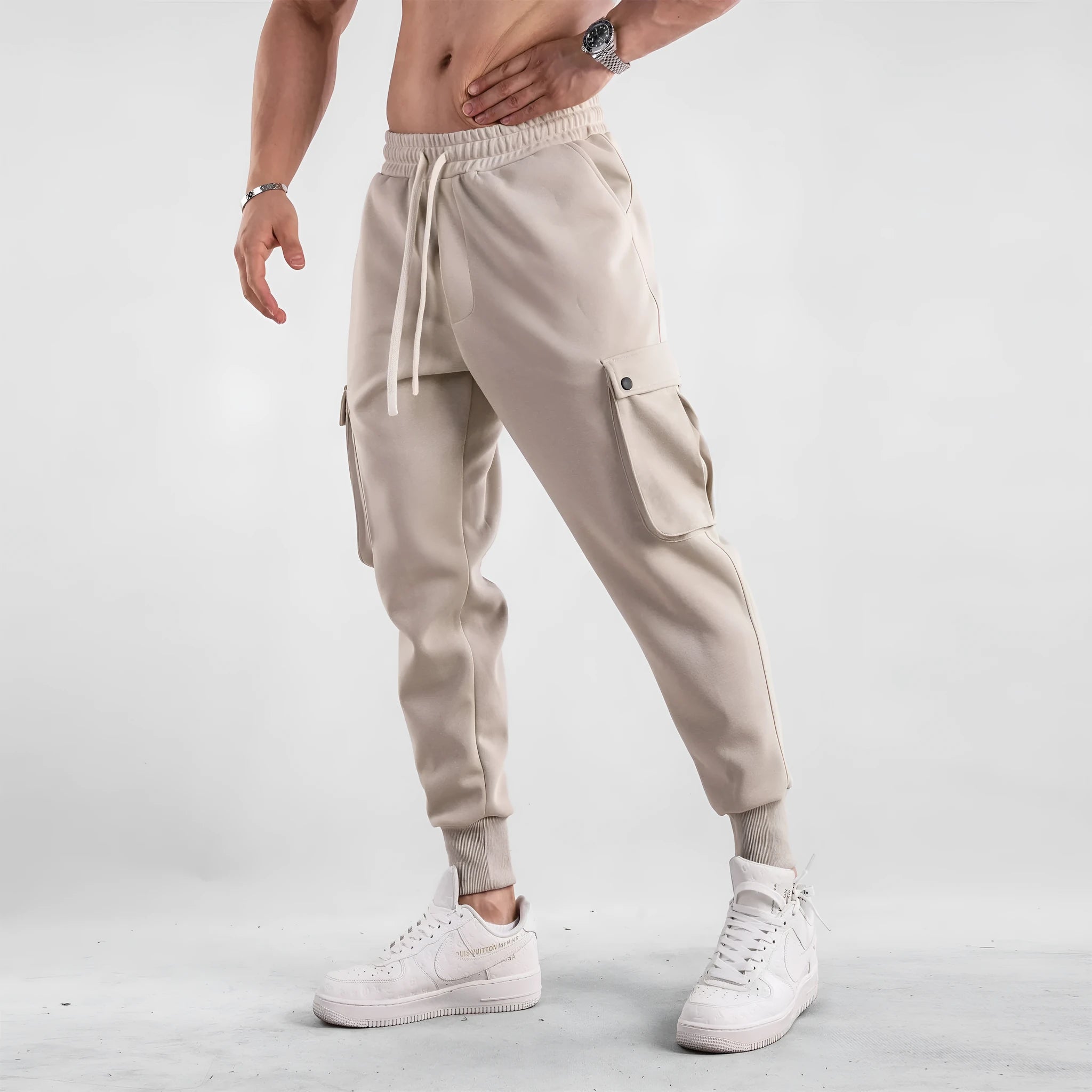 Men's loose-fit beige cotton sports trousers with ankle ties and side pockets laid flat.