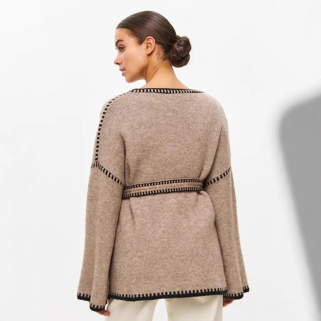 A white lace-up knitted cardigan with long sleeves on a hanger, showing the front tie detail.