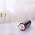 Black portable ultrasonic humidifier with colourful LED lights on a car cup holder.