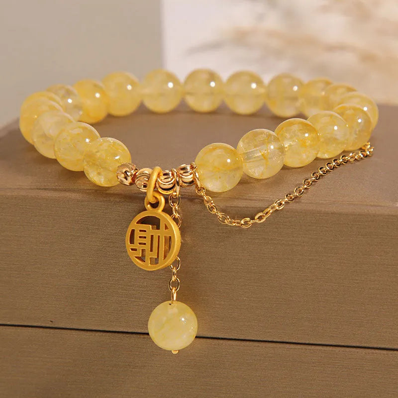 Women's natural citrine bracelet with a gold-tone Chinese character charm and tassel on an adjustable chain.