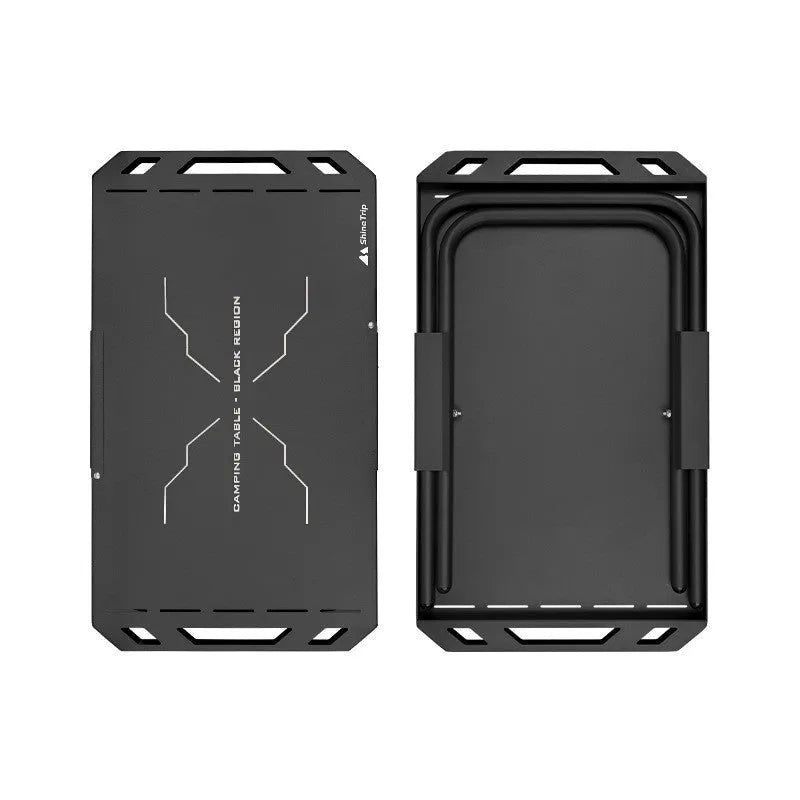 Black folding portable steel camping table on grass with storage bag beside it, 600x350x375mm dimensions visible