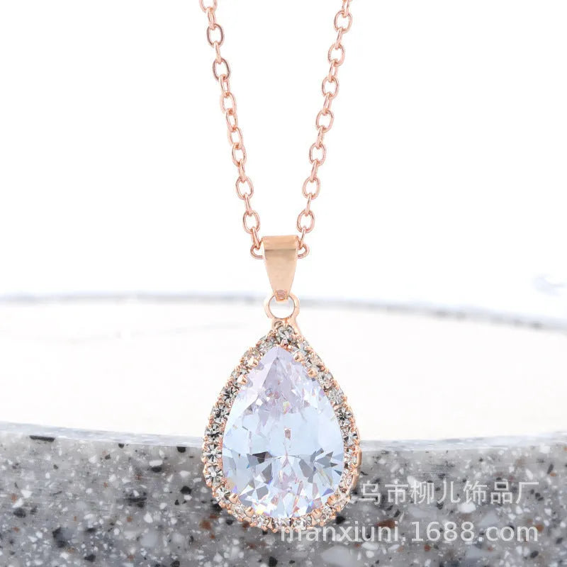 Close-up of a women's rose gold tone drop pendant necklace with pink rhinestone inlay on a model.