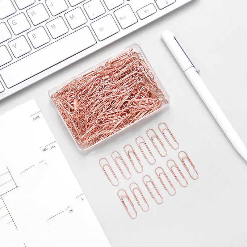 Box of 100 rose gold heart-shaped steel paper clips on a white background.