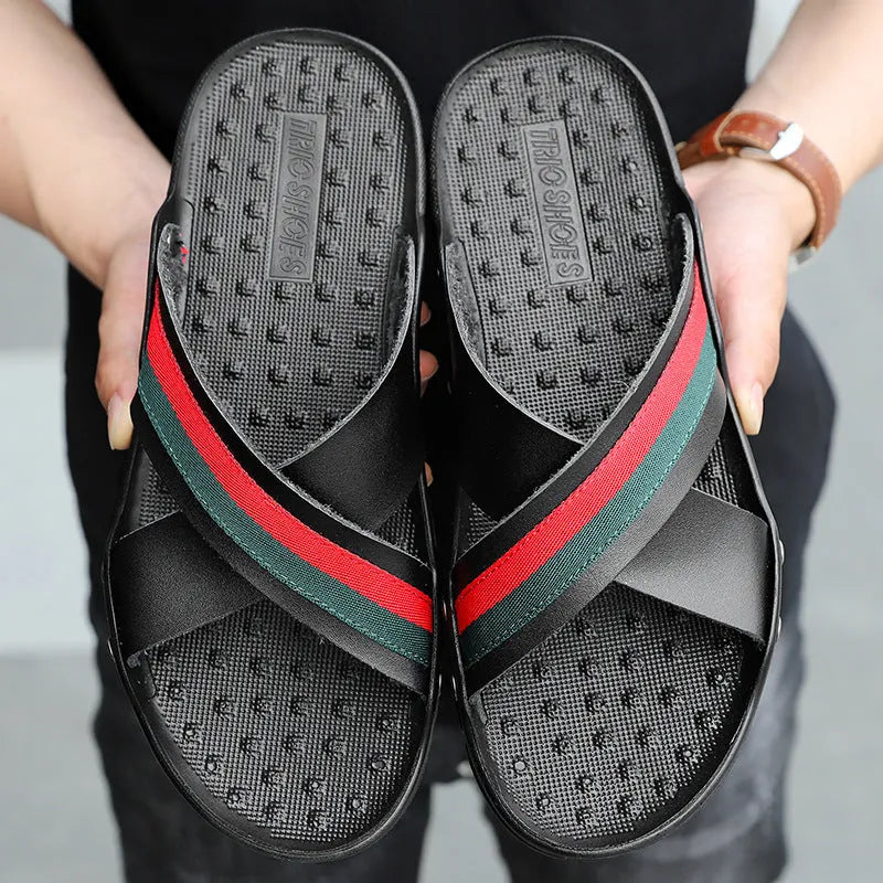 Men's black cowhide flip-flops with a textured non-slip PU sole on a sandy beach.