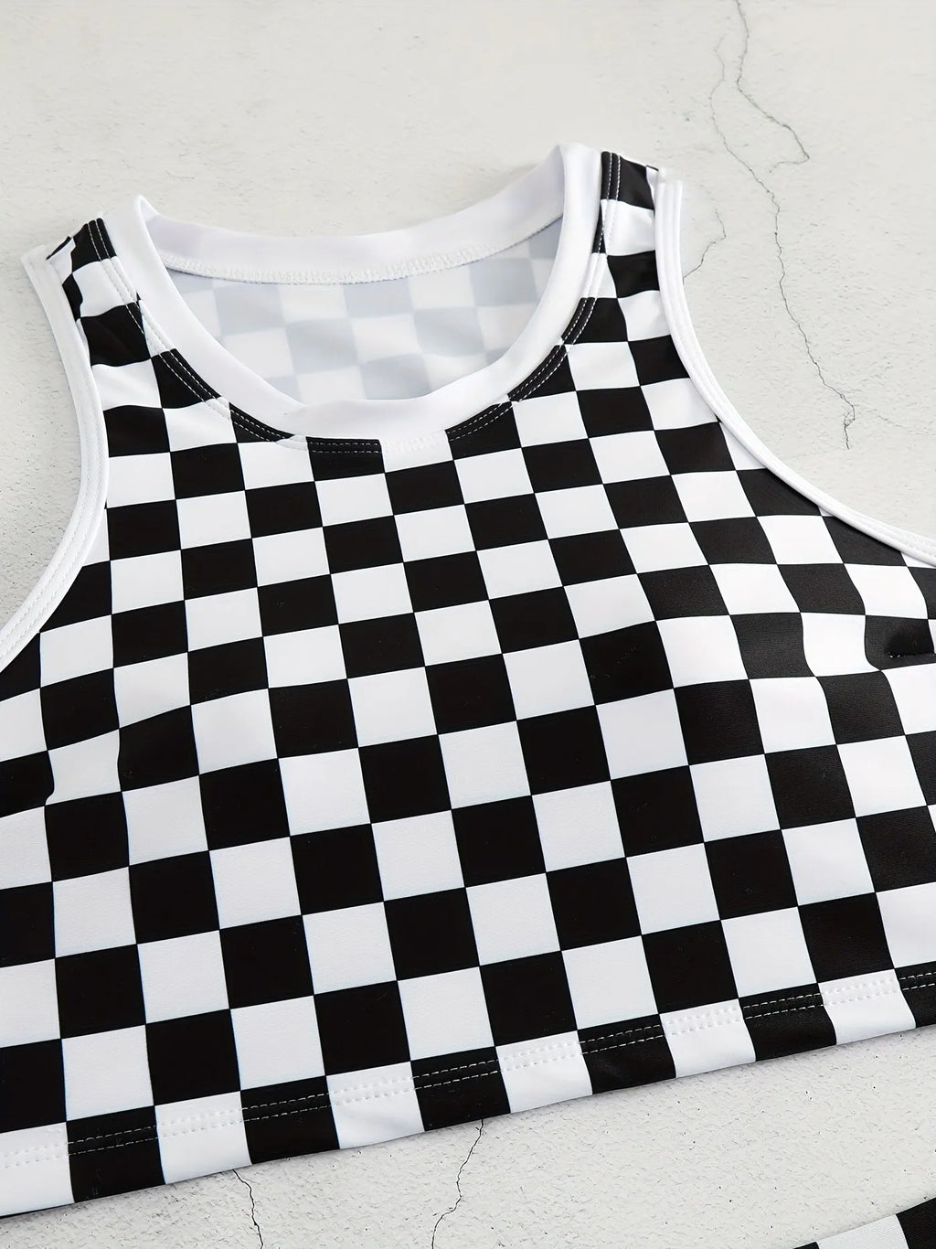 Backless one-piece women's swimsuit with black and white chessboard plaid pattern and white suspender straps.