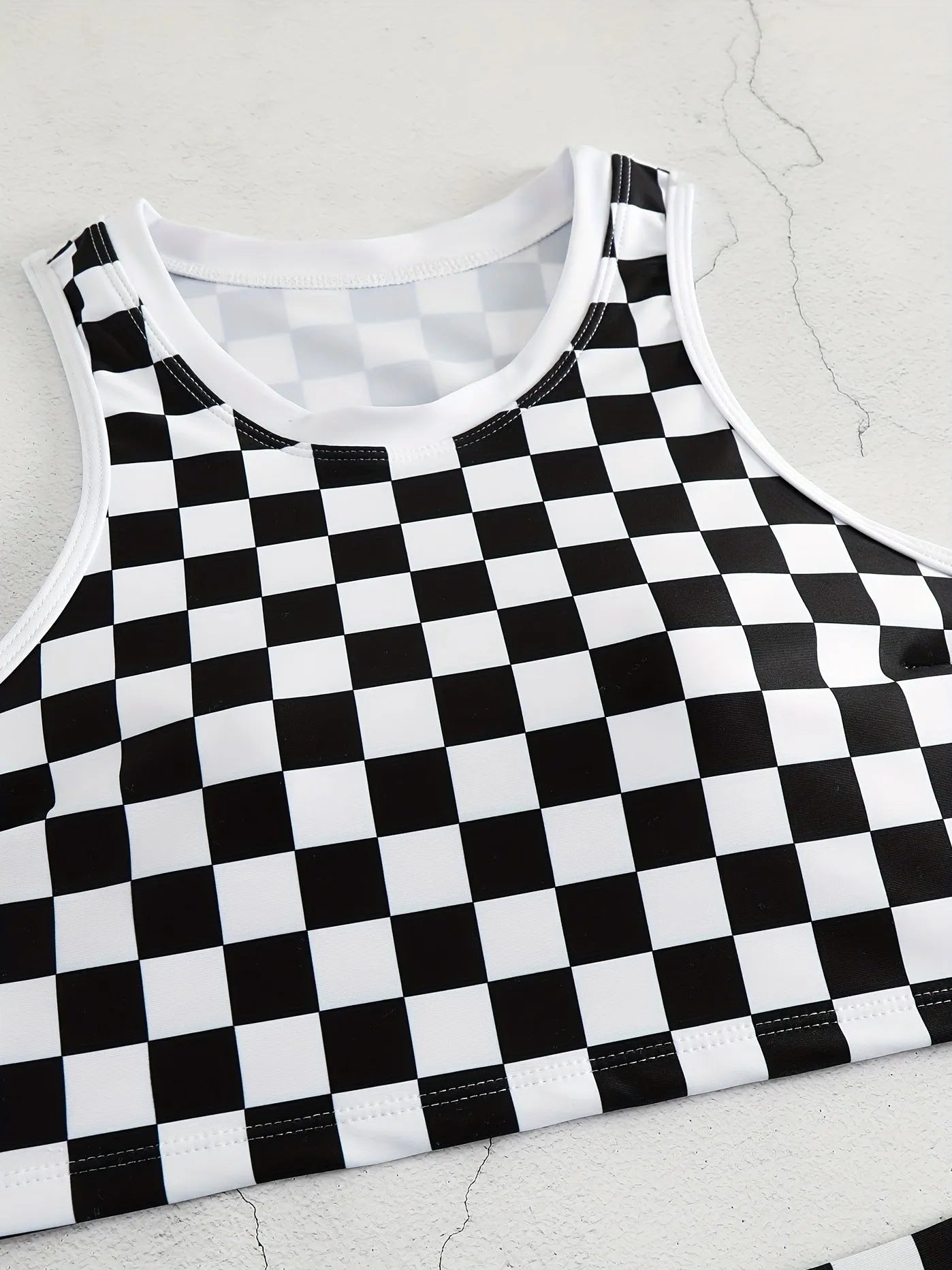 Backless one-piece women's swimsuit with black and white chessboard plaid pattern and white suspender straps.