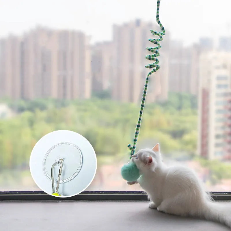 Spring-mounted cat toy with bell stick and inflatable ball, attached to a door via suction cup.