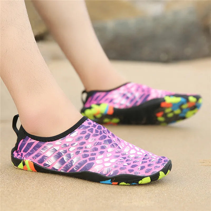 Blue and black Lycra fabric beach wading shoes with EVA foam soles on a sandy background.