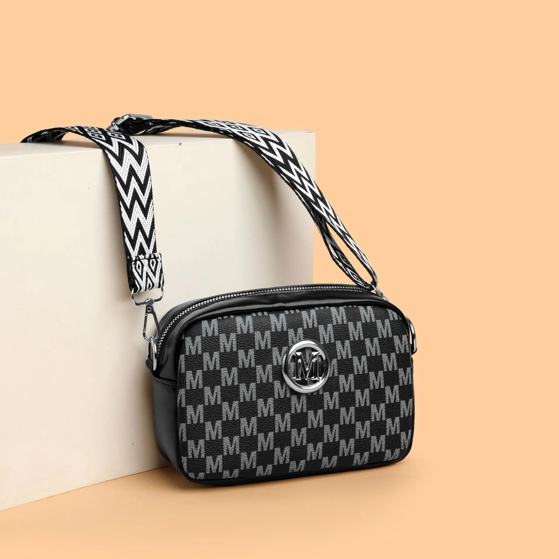 Black crossbody bag with wide strap and a three-dimensional front pocket.