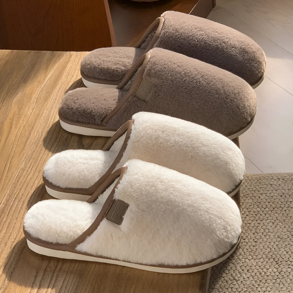 A pair of solid colour winter plush slippers with a PVC sole on a wooden floor.