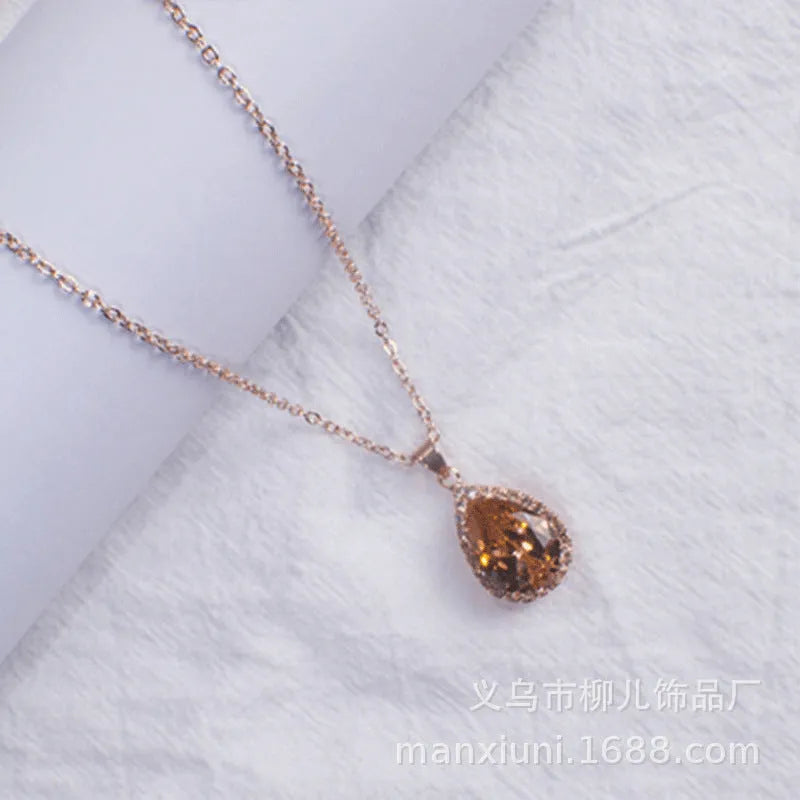 Close-up of a women's rose gold tone drop pendant necklace with pink rhinestone inlay on a model.