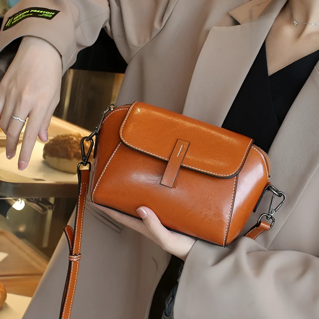 Brown leather women's crossbody messenger bag showing shell shape and visible stitching.