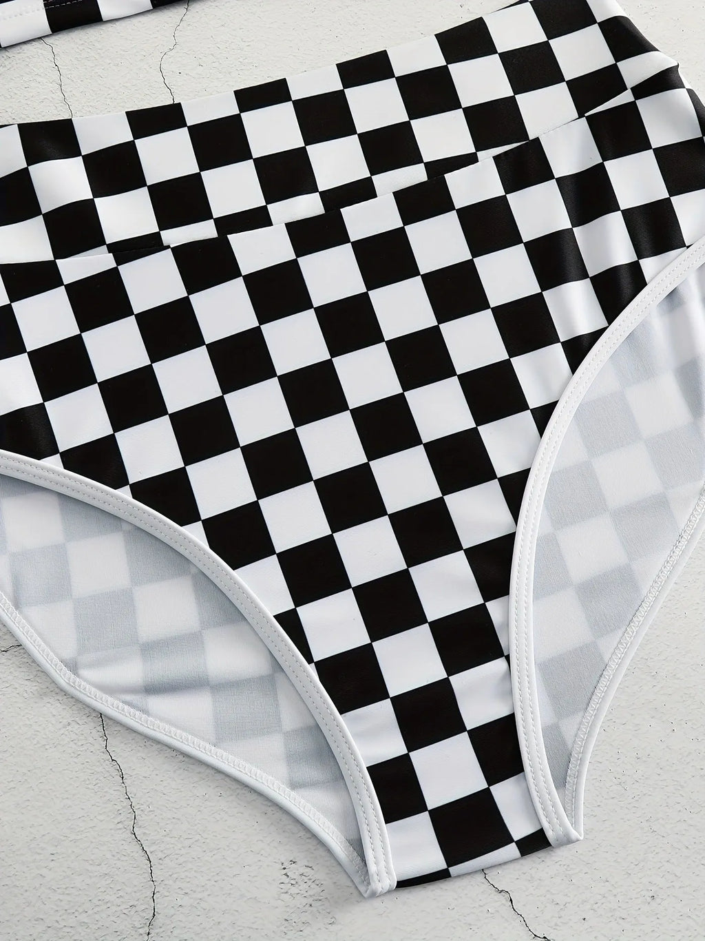 Backless one-piece women's swimsuit with black and white chessboard plaid pattern and white suspender straps.