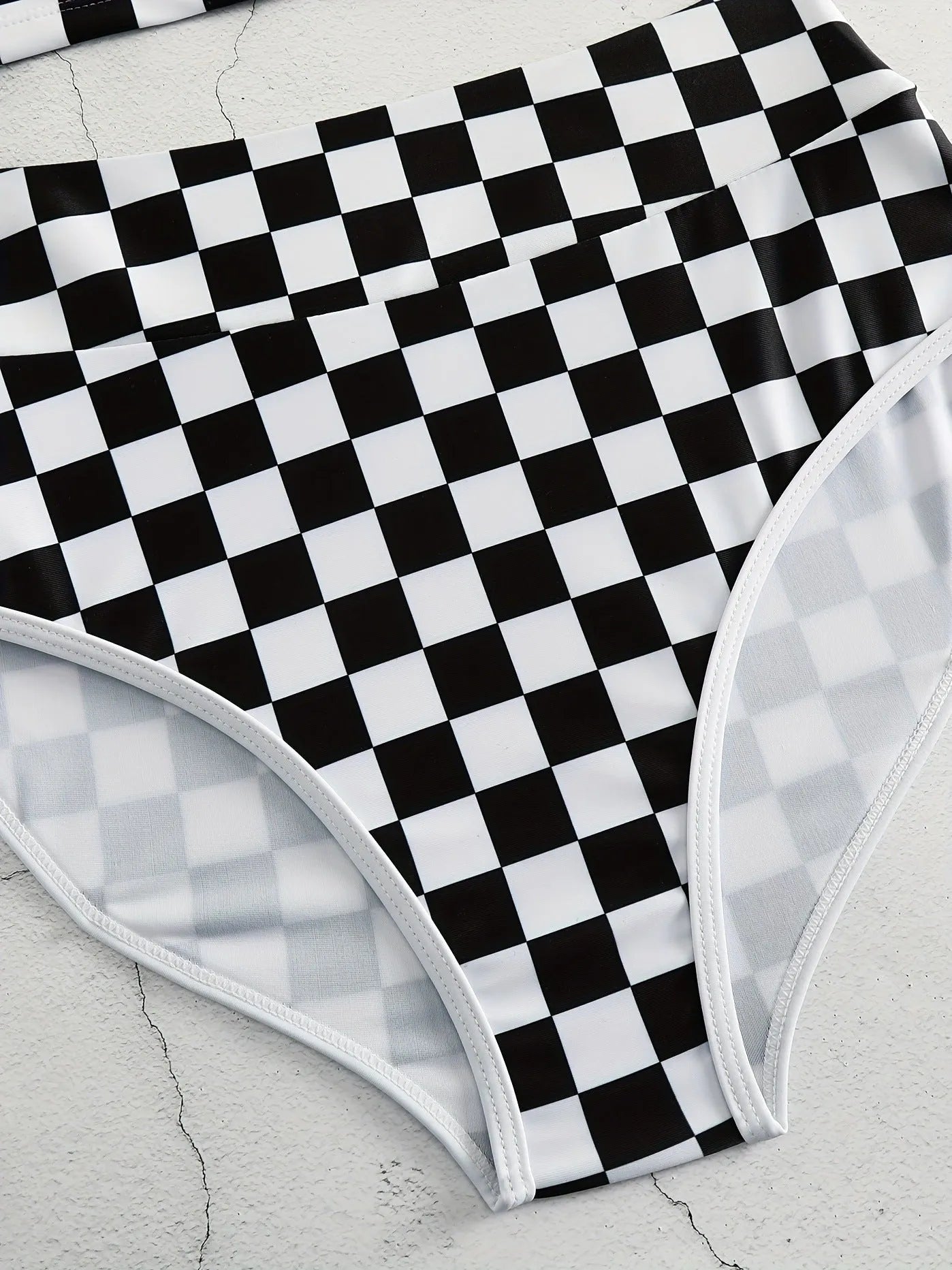 Backless one-piece women's swimsuit with black and white chessboard plaid pattern and white suspender straps.