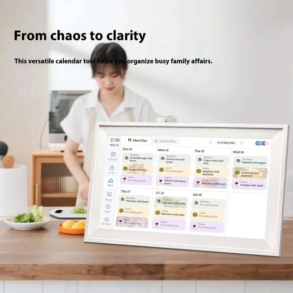 White 15.6 inch smart digital photo frame on a table showing a family photo, with mobile app upload icon.