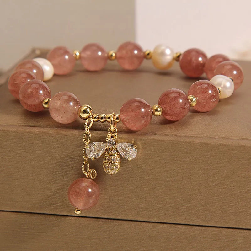 Women's bracelet with strawberry quartz pearls, a zircon bee charm, and alloy links on a wrist.