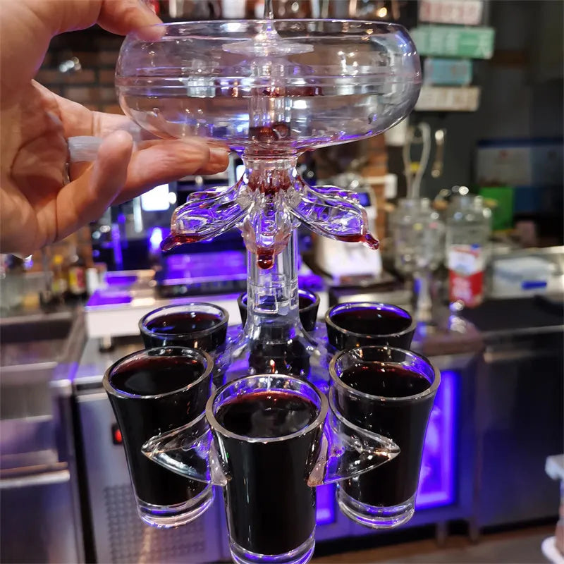 Transparent six-cup shot glass dispenser rack with gold-trimmed cups on a table.