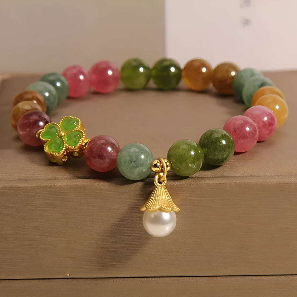 Close-up of a women's silver-toned bracelet with a four-leaf clover charm, pearl pendant, and colourful tourmaline stones.