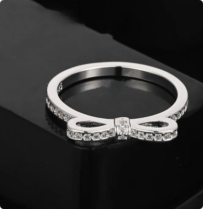 Silver bow-shaped ring with sparkling rhinestones and zircon crystals on a finger.