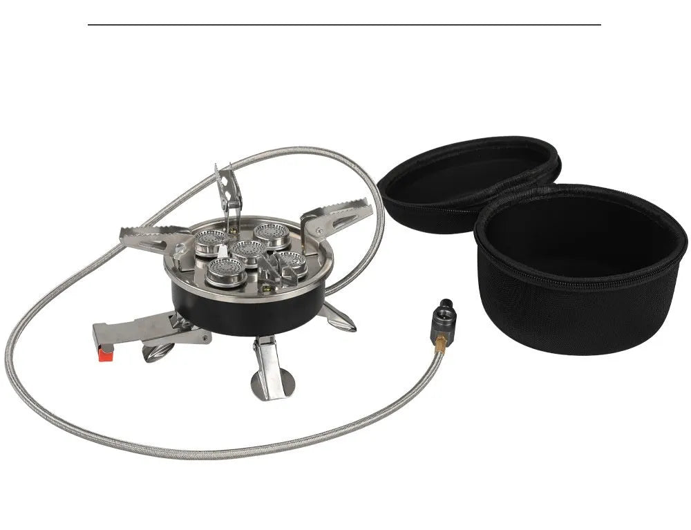 Silver portable split camping stove with foldable legs and a long black hose, on a grass background.