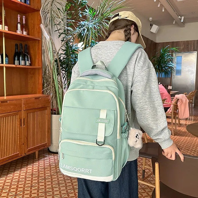 Nylon school backpack in green with pendant, showing curved shoulder straps and sewing line detail.