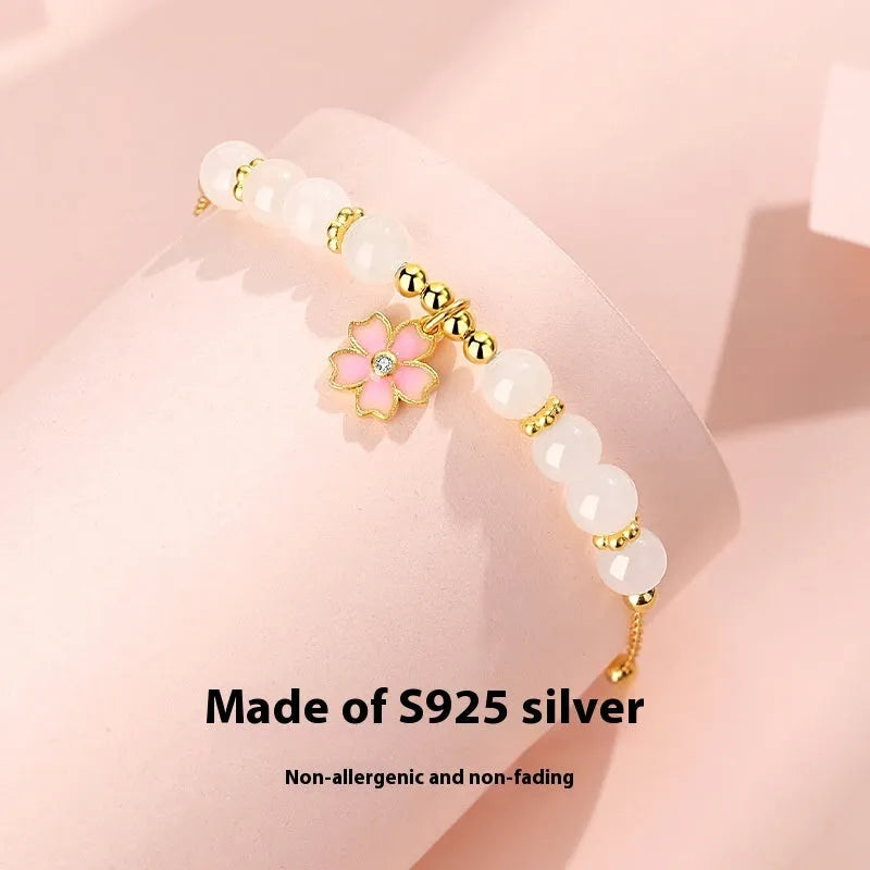 Close-up of a women's pink cherry blossom pendant and Hetian jade bead bracelet made from S925 silver.