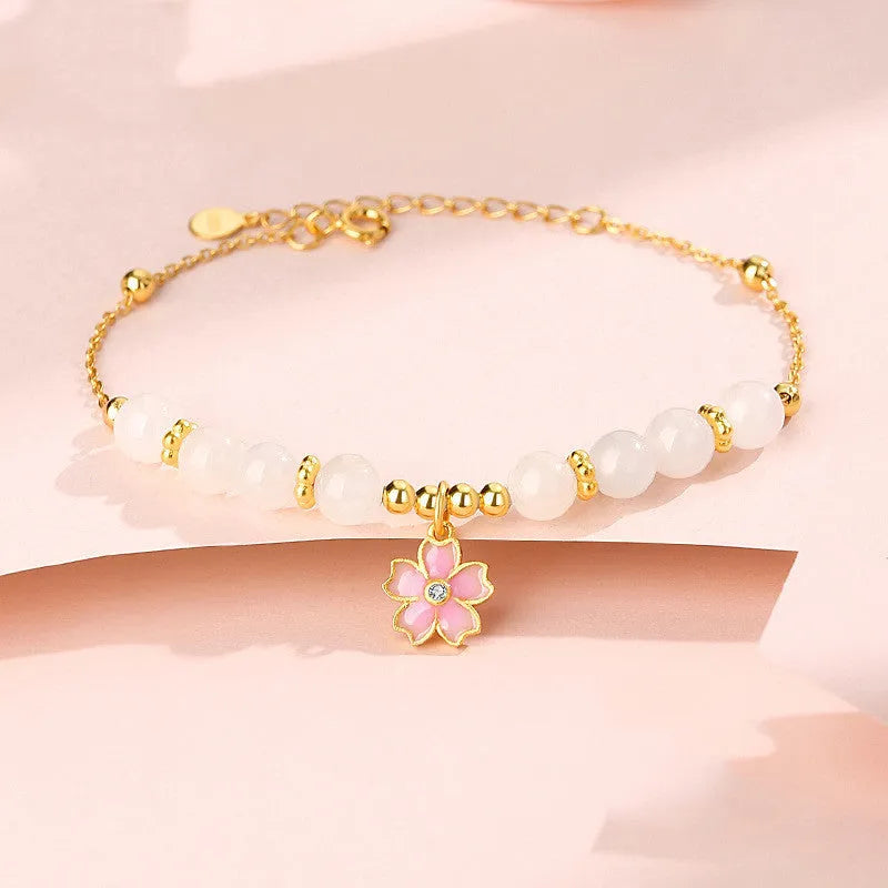 Close-up of a women's pink cherry blossom pendant and Hetian jade bead bracelet made from S925 silver.