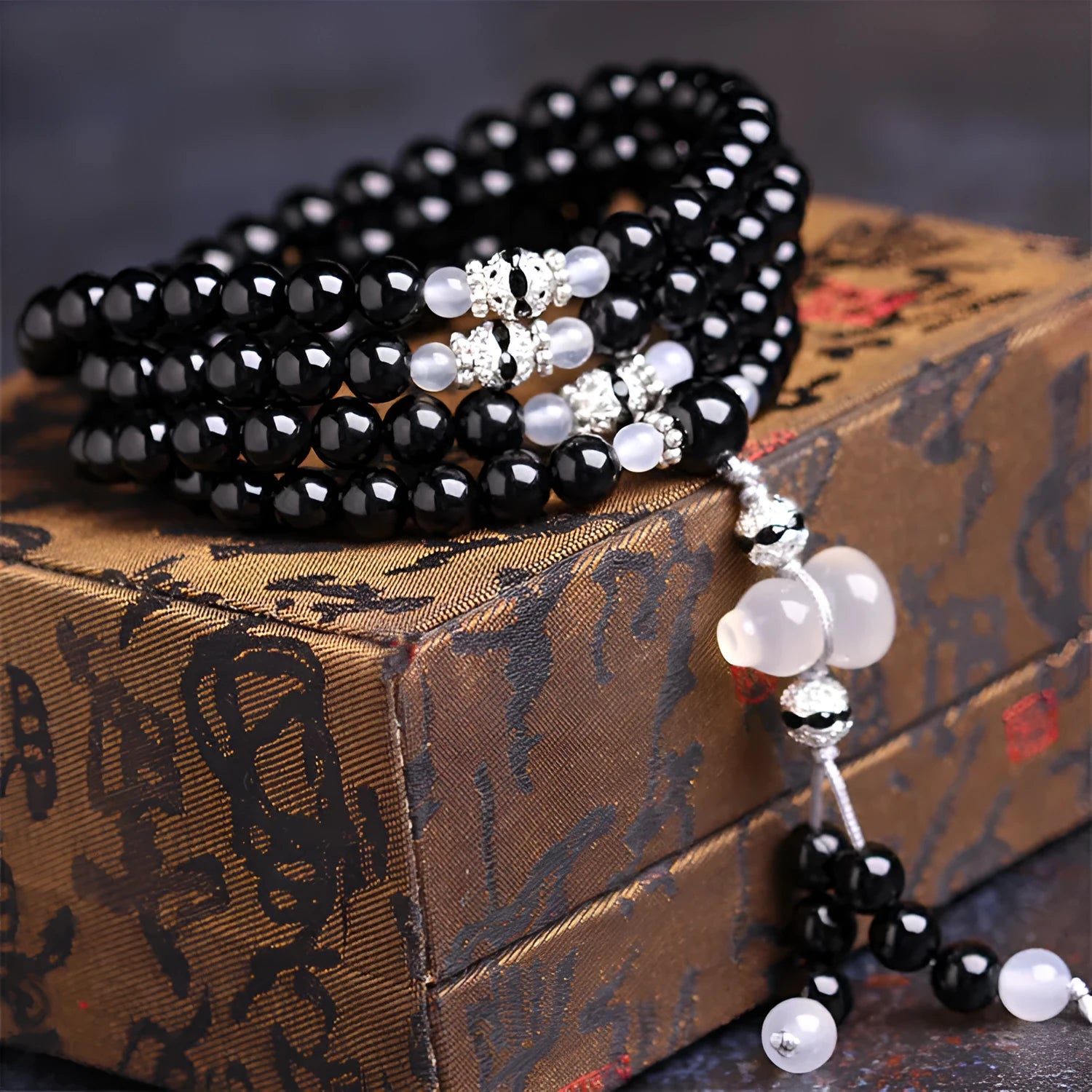 Natural black and red agate 108 bead bracelet with geometric shapes on a wrist.