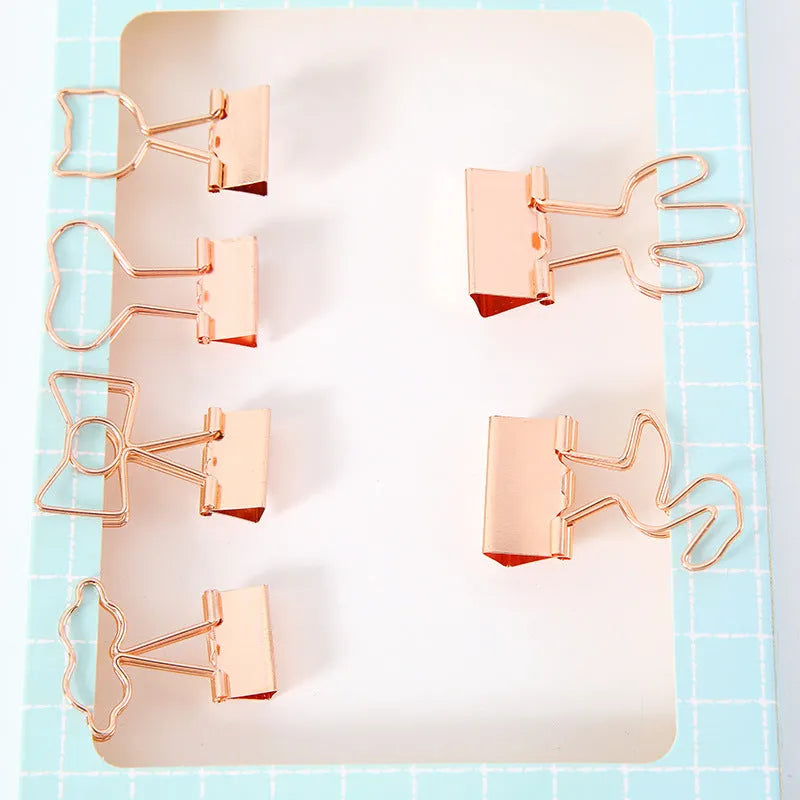 Gold metal decorative paper clips in shapes of a flamingo, a cat, a cactus, a bow, a love symbol, and clouds.
